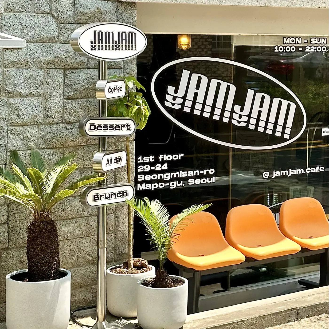 JAMJAM 타원 간판과 Coffee·Dessert·All day·Brunch 방향 표지판, 오렌지 벤치가 놓인 성미산로29길 24 매장 앞